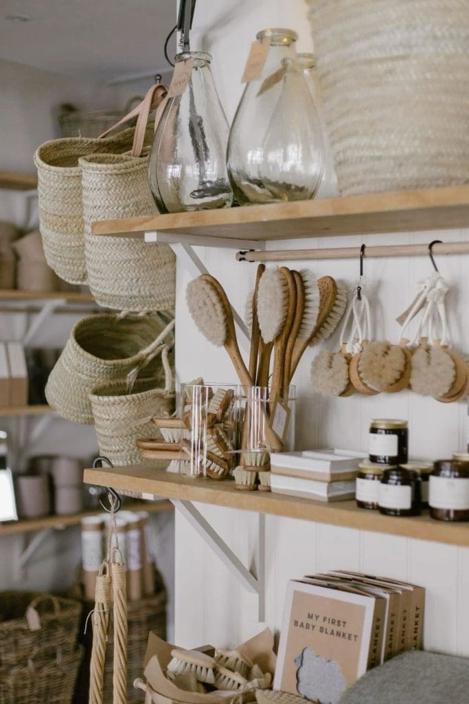 Sustainable and Environmentally Friendly Design image of small artisan shop shelves featuring hand woven straw basket bags, wooden handle body brushes, small glass jar candles and recycled glass jars