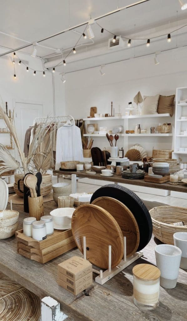 Sustainable and Environmentally Friendly Design image of small artisan store with wooden carved dinner plates, small glass jar candles, wooden serving spoons and white and camel coloured linen decorative cushions