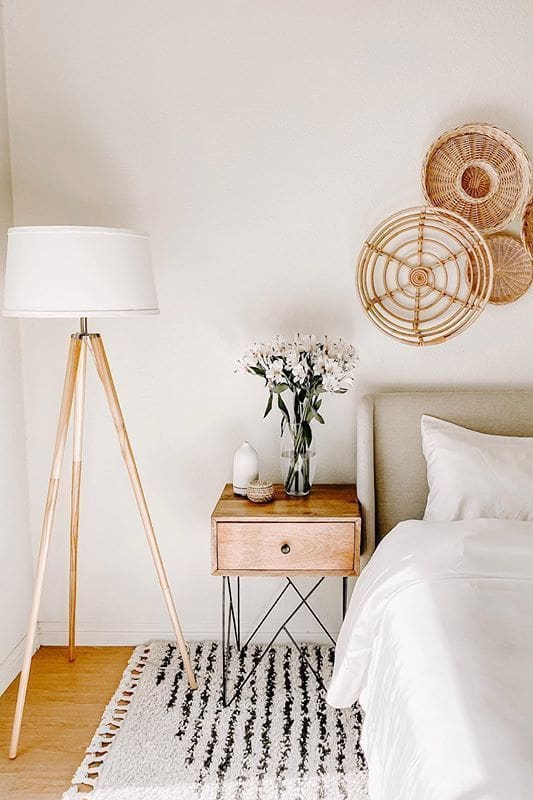 Biophilic Interior Design image of bedroom with white walls, tripod floor lamp with white shade and woven basked wall decor