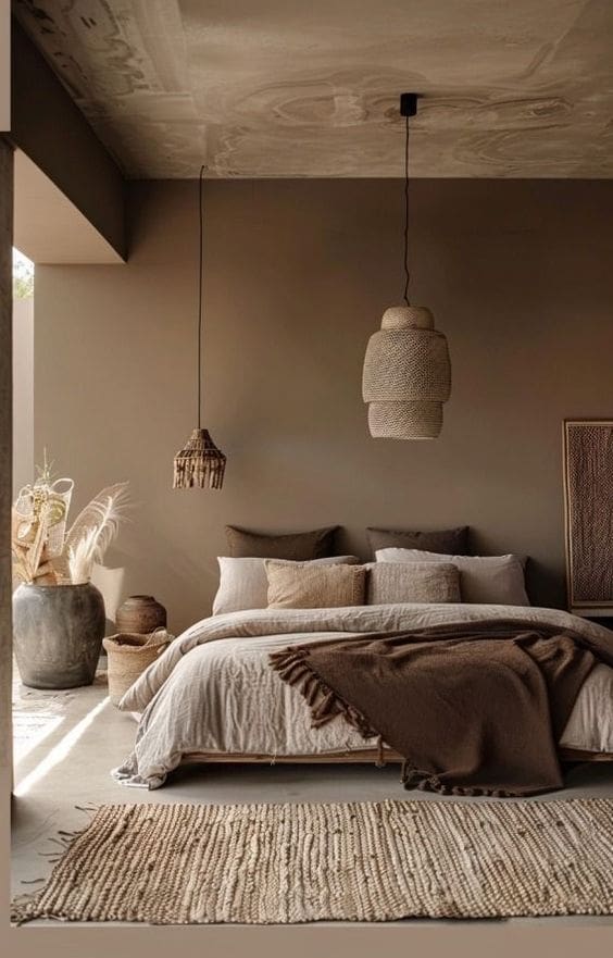 Brown colour drench bedroom showcasing bed with overhead pendant lighting, throw pillows, rug and larfe floor vases all in varying shades of brown