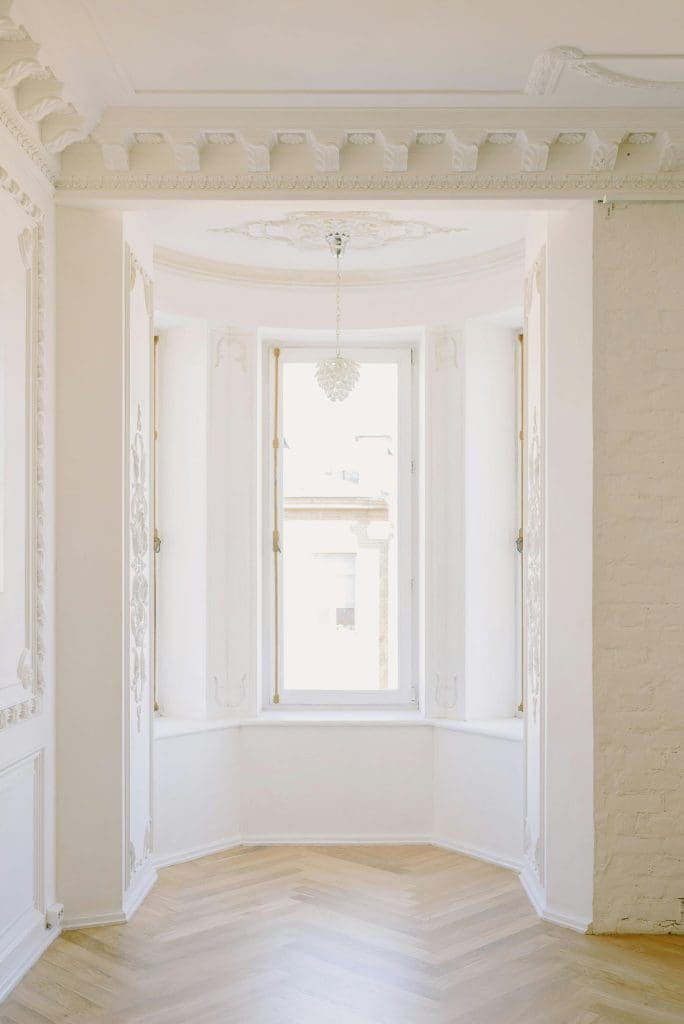 Biophilic Interior Design image of large Georgian style bay window with white washed walls, decorative ceiling details and light wood parquet style flooring