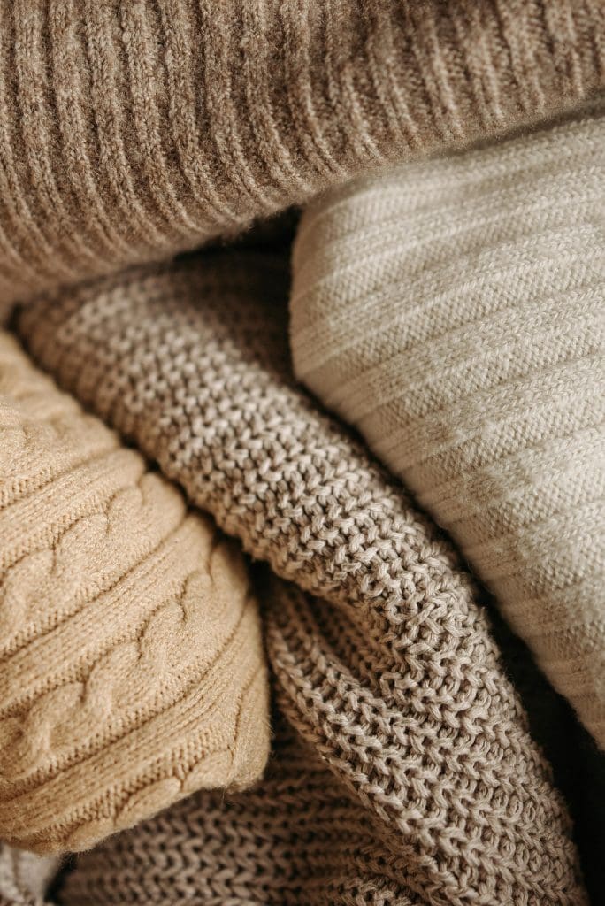 collection of knitted throws roughly folded in oatmeals, creams, beiges and caramel colours