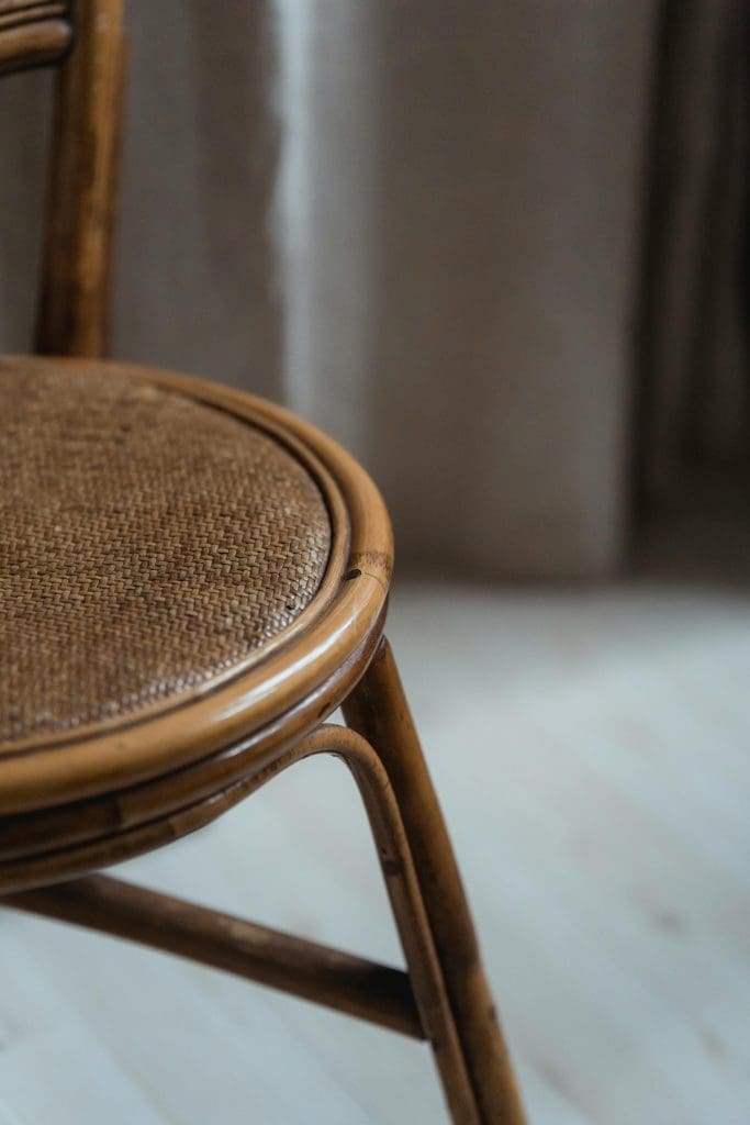 side profile of a vintage chair in warm dark brown wood tone and woven rattan seat bottom