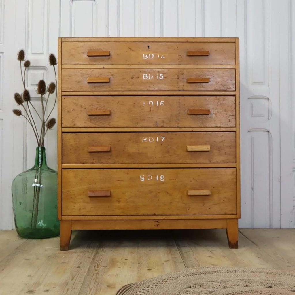 Mid-Oak tall chest of drawers with school numbering to the front. Style with green glass vase and dried flowers