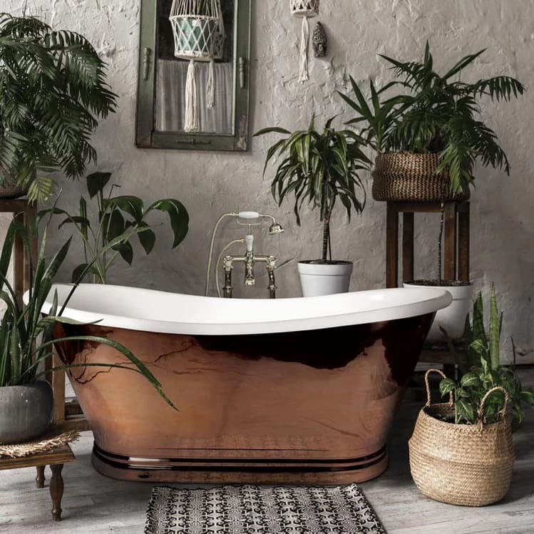 Copper plated roll top bath with rustic platered walls and lots of plants around in wicker woven baskets