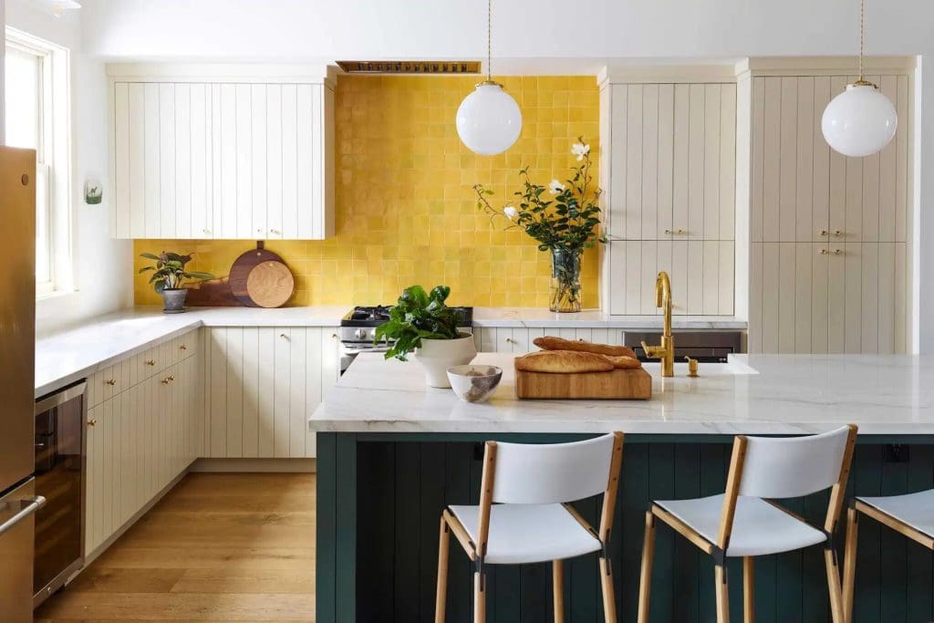 Large open plan kitchen with off-white cabinets, yellow ochre splashback and large kitchen island painted dark forest green.