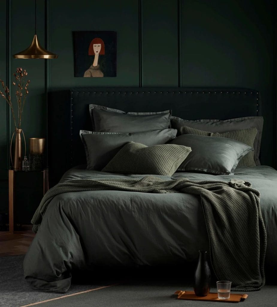 Dark and moody bedroom with dark green bedding, throws, walls and flooring. Accented with aged brass