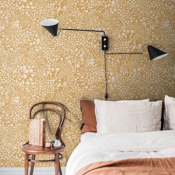 Bedroom wall with yellow ochre and white floral patterned wallpaper, vintage cafe wooden chair and relaxed bedding of white and terracotta linen.