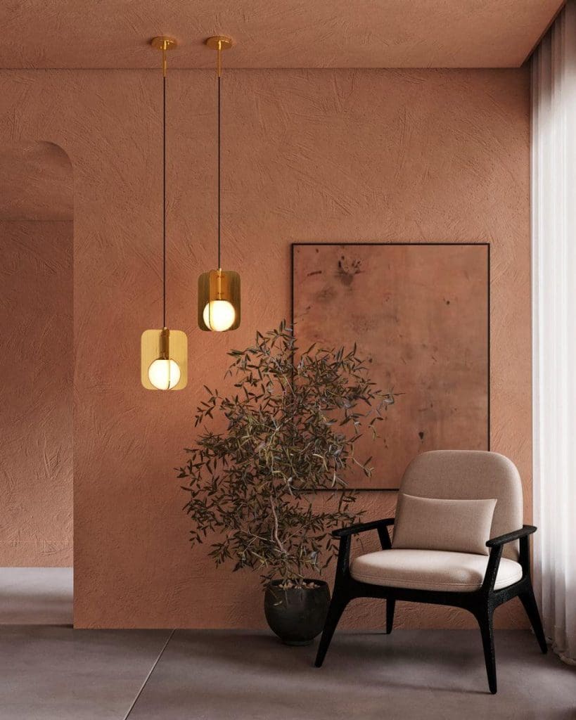 Distressed terracotta painted walls and ceiling styled with gold hanging pendant bulbs, black framed occasional chair and small olive tree