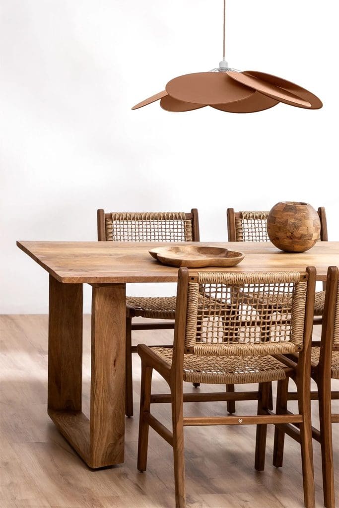 Terracotta disk patterned ceiling pendant over wooden chunky table and rustic wood and woven rattan chairs