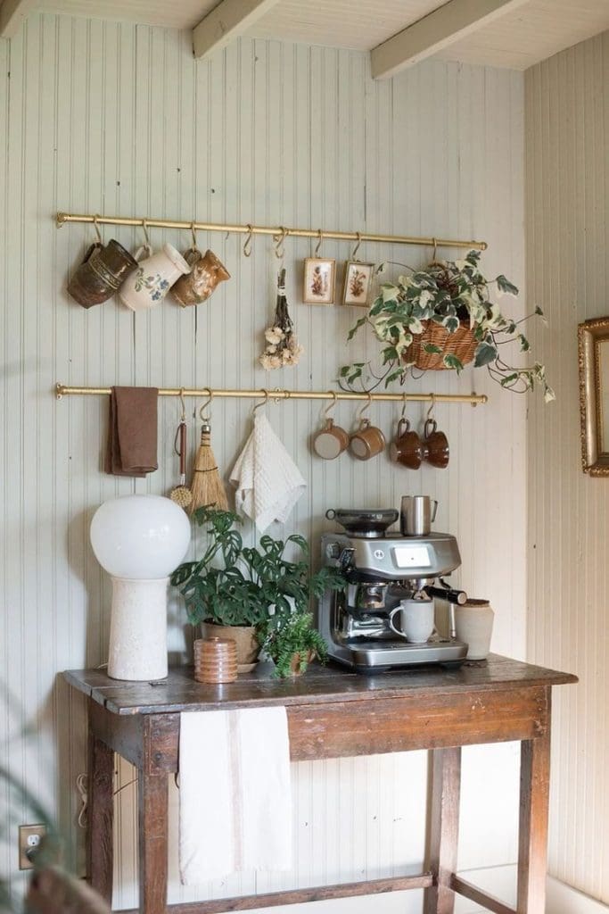 Repurposed vintage side table with traditional wooden wall panelling and brass rail and hook stying for cups, teatowels and tools.