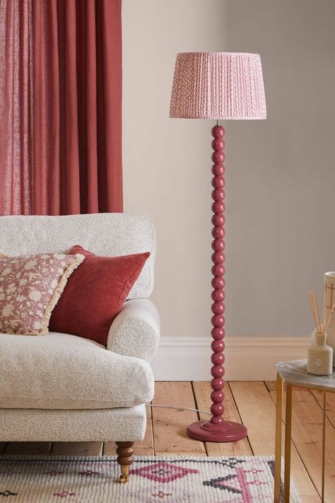 Red bobbin design floor lamp with ruffled lampshade on bare wood flooring