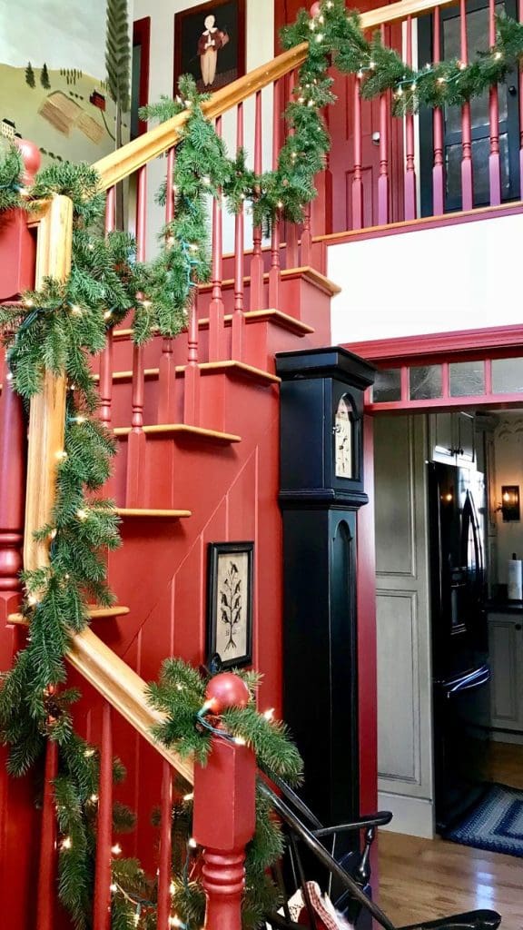 Red painted staircase with green garland and black modern style grandad clock