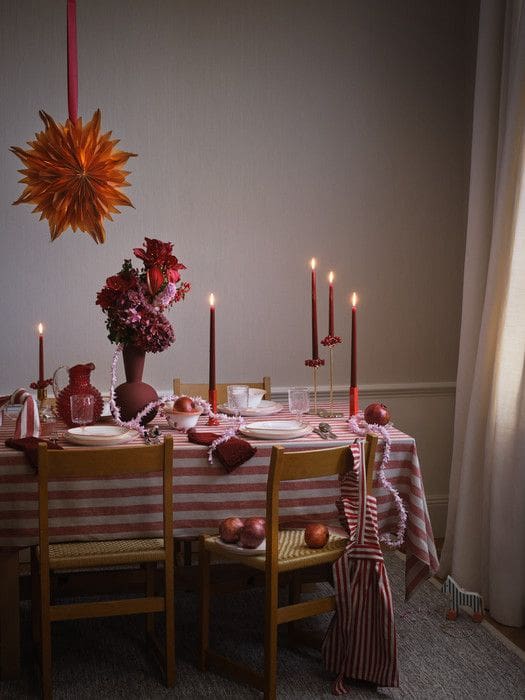 Christmas tablescape with red stripe tablecloth, red pillar candles and warm wood simple chairs