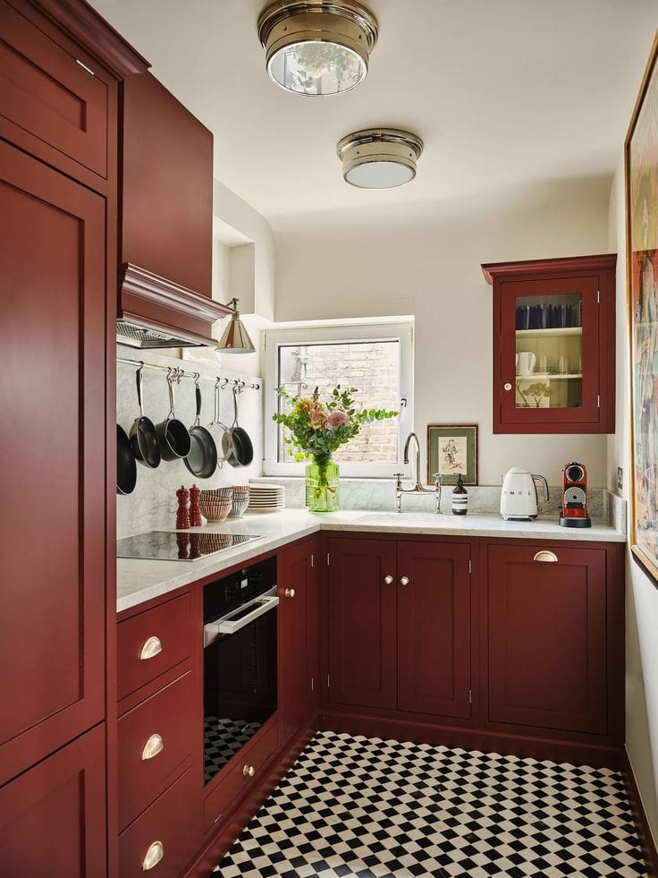 Deep red kitchen cabinetry with off-white walls and blakc and white checked floor