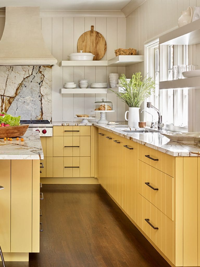 Kitchen with wood panelled wall detail and marble splashback. Kitchen cupboards painted in a buttery yellow and black hardware