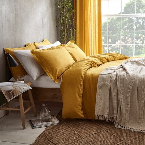 A bedroom space styled with yellow linen bedding, jute woven rug and light grey limewashed walls