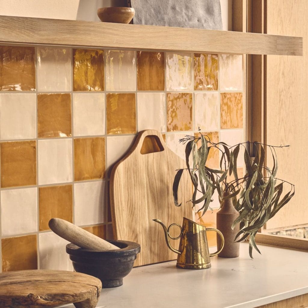 Yellow and off-white square checkerboard patterned tile splash back with warm light oak wood floating shelf above