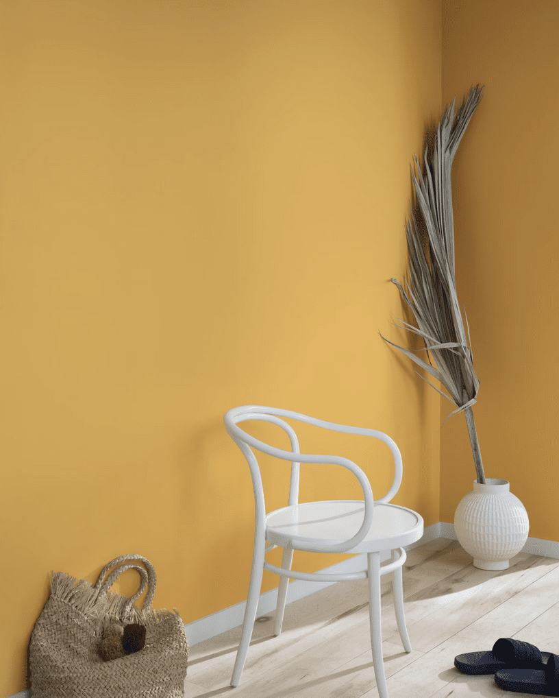 Warm golden yellow painted walls with a stark white cafe chair and sisal woven basket with plated handles