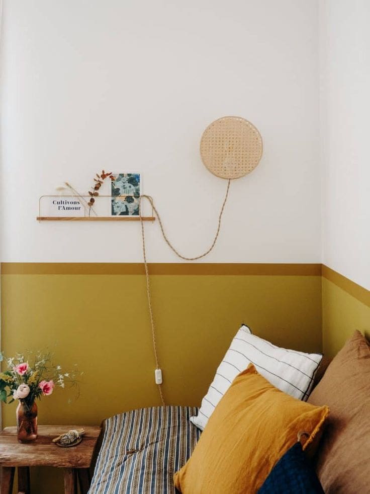 Half painted wall in white at the top and ochre yellow to the bottom. Day bed against wall with various striped and plain throw pillows and cushions